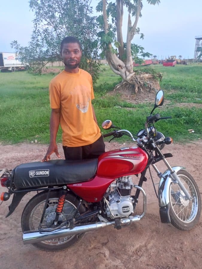 A young man standing beside the motorcycle he received through the programme